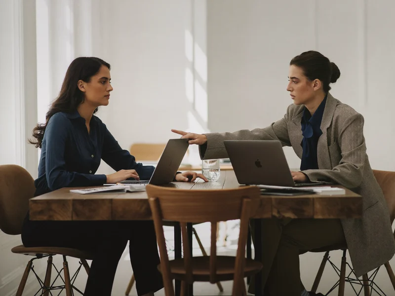Zwei Lernende diskutieren nebeneinander am Tisch über Inhalte auf dem Laptop